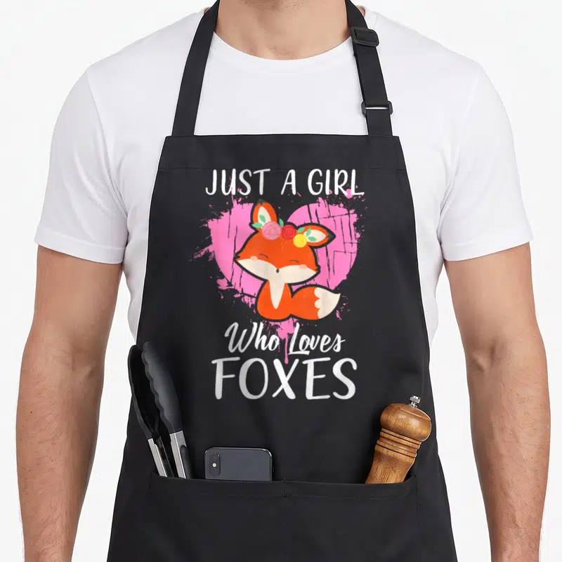 Funny fox print apron - Cartoon orange fox with flower crown in front of pink heart and white text — shown on a black cotton canvas apron against a white background