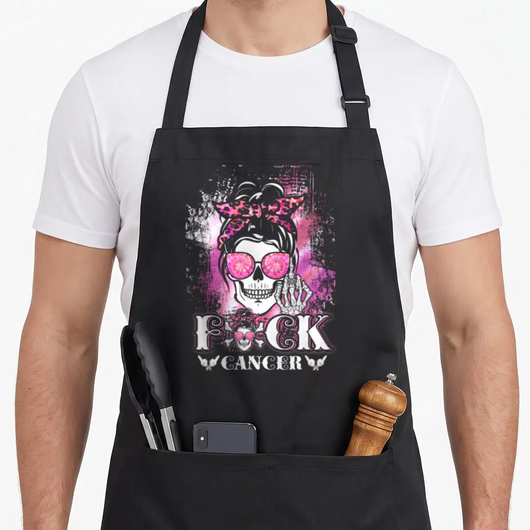 Breast skull apron - Skeleton head wearing sunglasses and bandana withFuck Cancer text and ribbons — shown on a black cotton canvas apron against a white background
