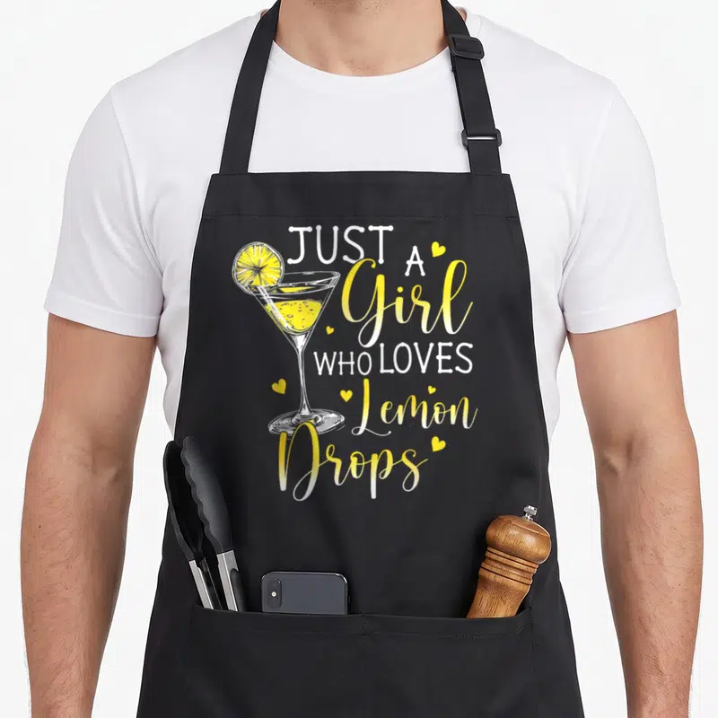 Drop drink for love and lemons apron - Cocktail glass with lemon slice and white yellow text reading Just A Girl Who — shown on a black cotton canvas apron against a white background