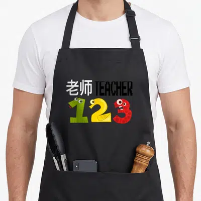 Esl teacher apron - Bilingual teacher text above green yellow red monster numbers 1 2 3 — shown on a black cotton canvas apron against a white background