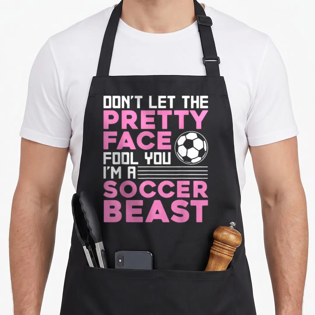 Sport soccer player accessories apron - Stacked pink and white text reading DON'T LET THE PRETTY FACE FOOL YOU I'M — shown on a black cotton canvas apron against a white background
