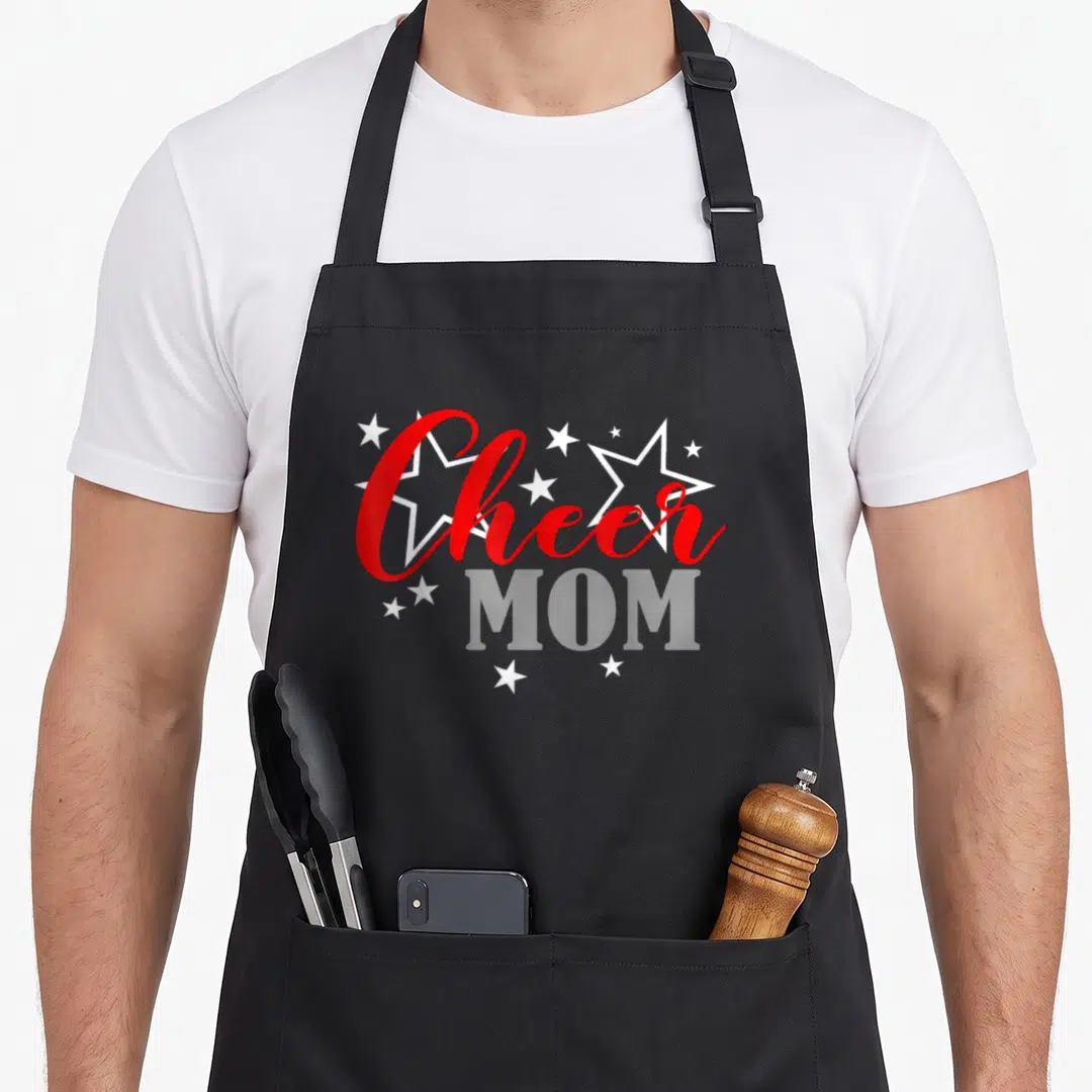 Cheerleader pride apron - Red script Cheer above grey MOM text with scattered white stars on grey background — shown on a black cotton canvas apron against a white background