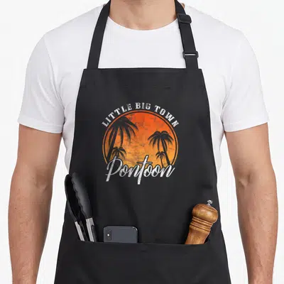 Pontoon summer aprons - Distressed LITTLE BIG TOWN text over orange sunset circle with four grey palm trees and Pontoon — shown on a black cotton canvas apron against a white background