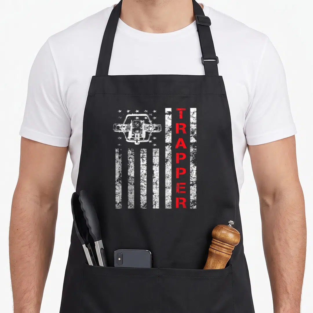 Trapping american flag apron - Distressed white truck and red vertical TRAPPER text over white stars and stripes — shown on a black cotton canvas apron against a white background