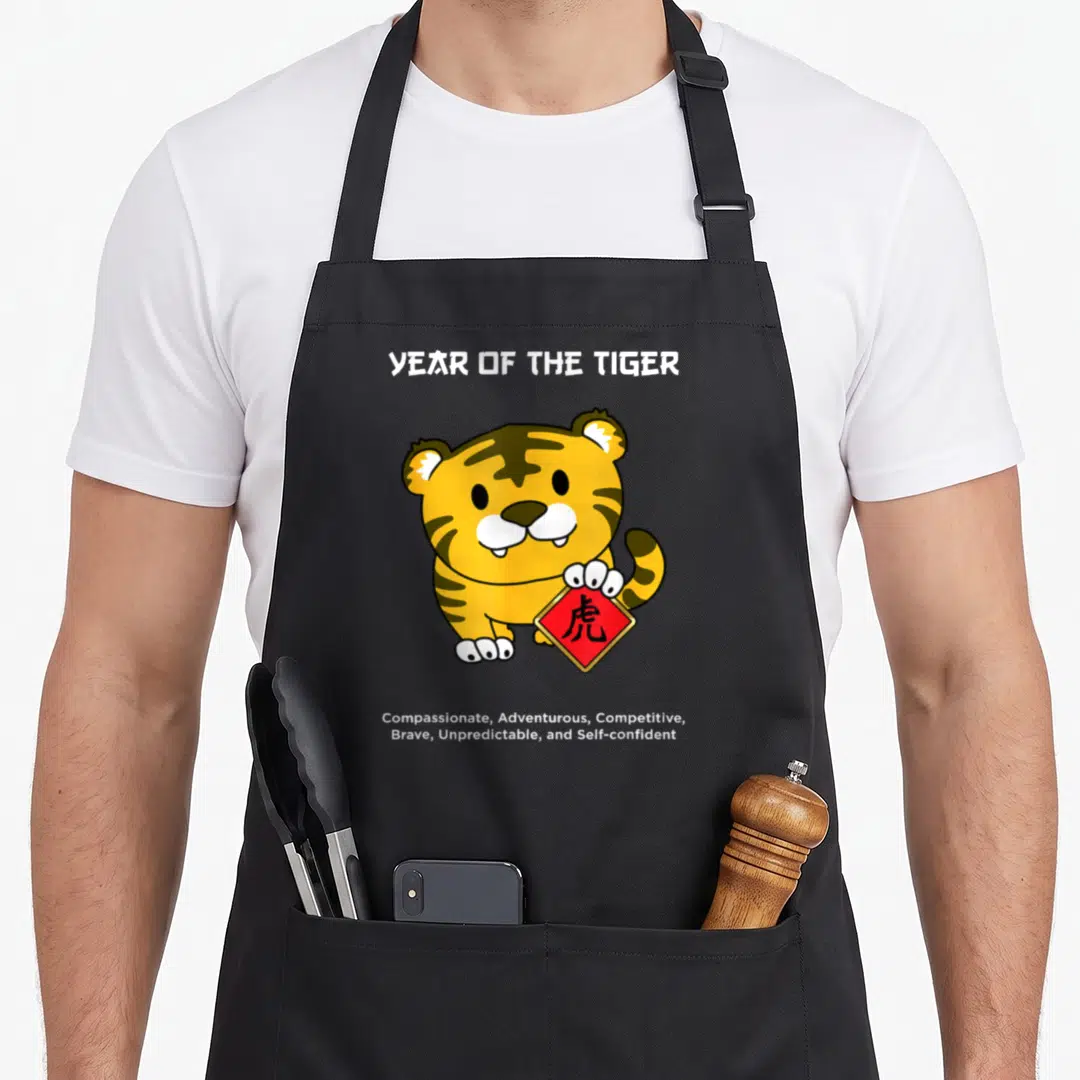 Tiger chinese zodiac aprons - Cartoon tiger holding red sign with character and list of personality traits — shown on a black cotton canvas apron against a white background