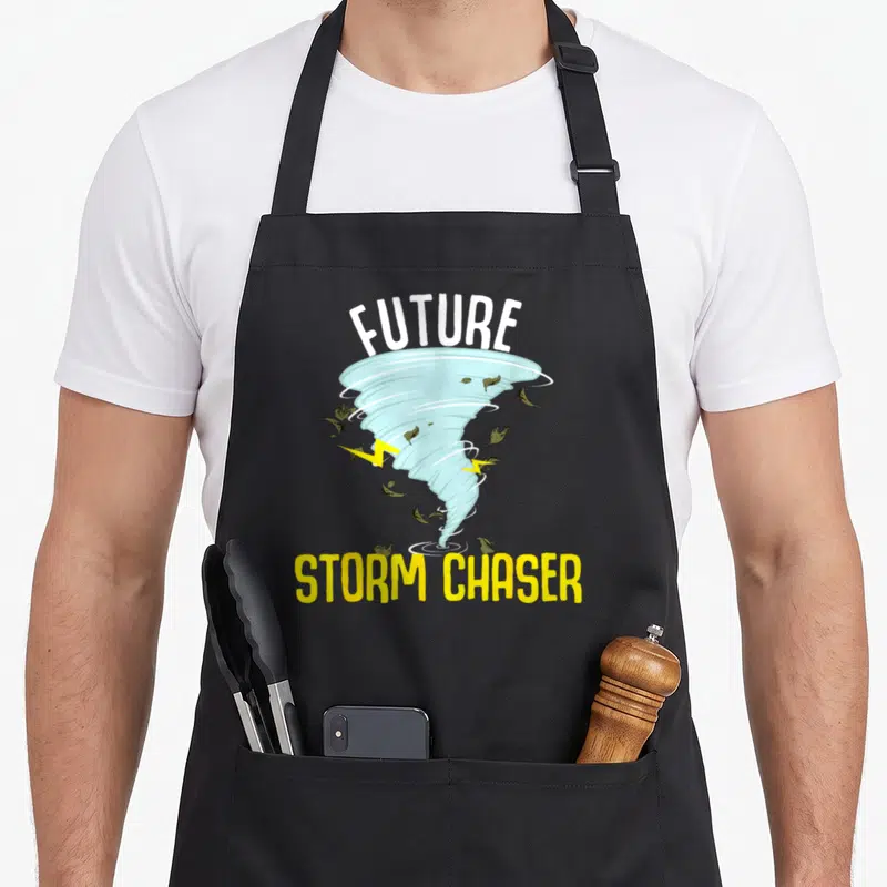 Future storm meteorologist apron - Cartoon light blue tornado with FUTURE STORM CHASER text and olive leaves — shown on a black cotton canvas apron against a white background