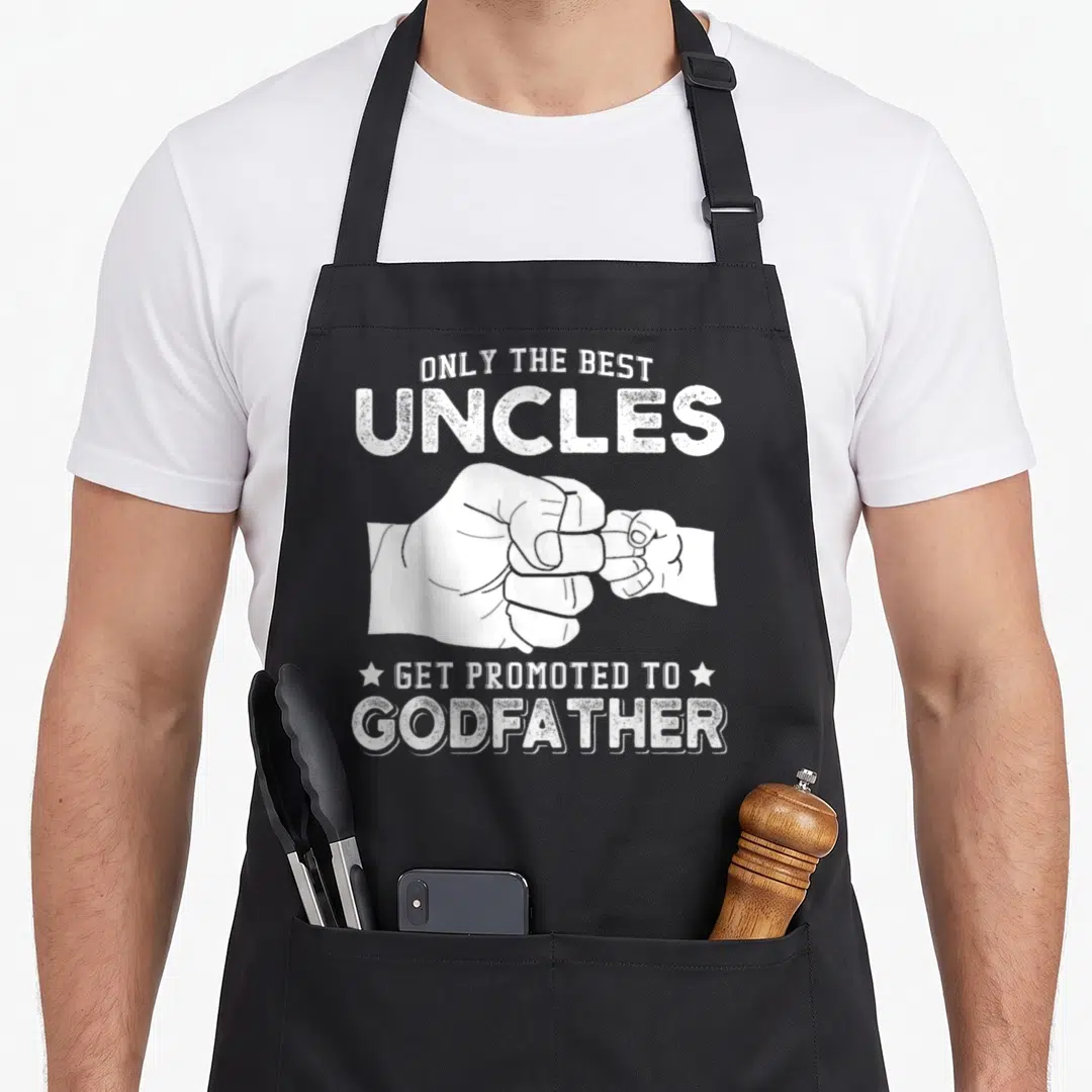 Uncle proposal apron - White distressed text reading Only The Best Uncles Get Promoted to Godfather above and below — shown on a black cotton canvas apron against a white background