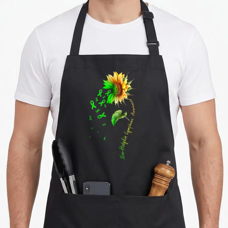 Non sunflower apron - Watercolor sunflower with green ribbons and Non-Hodgkin Lymphoma Awareness text — shown on a black cotton canvas apron against a white background