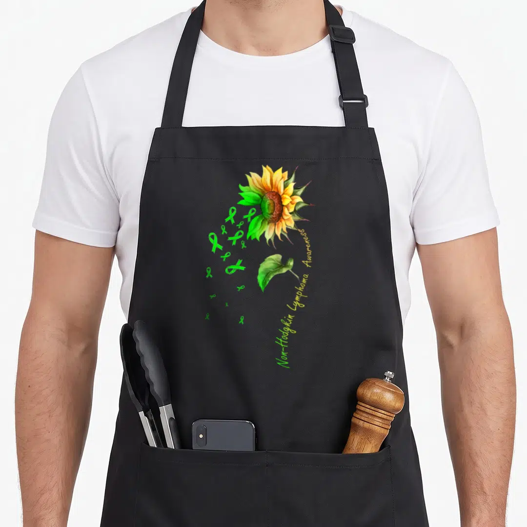 Non sunflower apron - Watercolor sunflower with green ribbons and Non-Hodgkin Lymphoma Awareness text — shown on a black cotton canvas apron against a white background