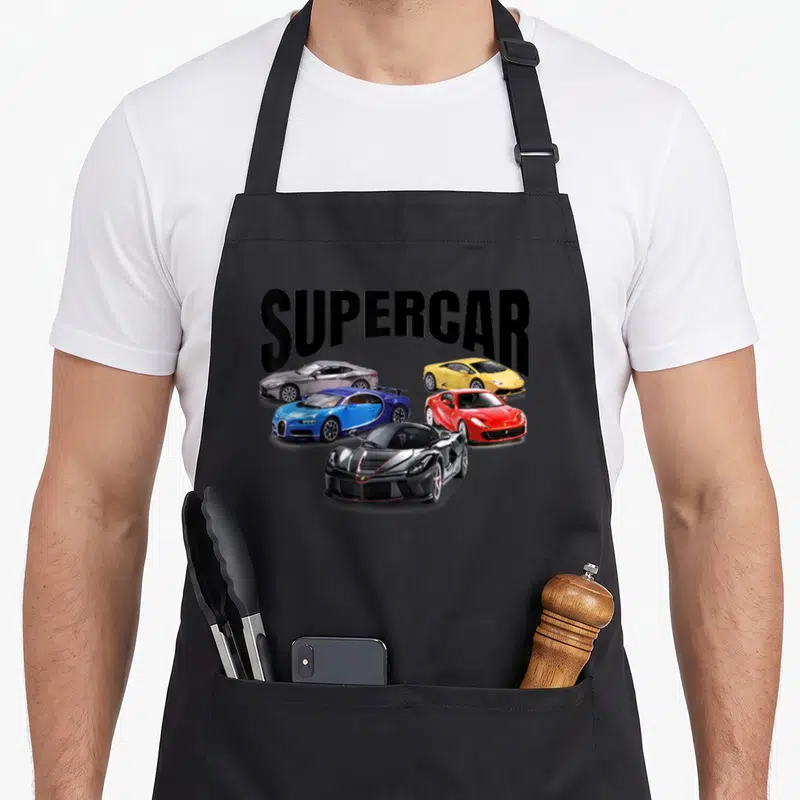 Supercar racing apron - SUPERCAR text above five red blue yellow silver and black sports cars — shown on a black cotton canvas apron against a white background