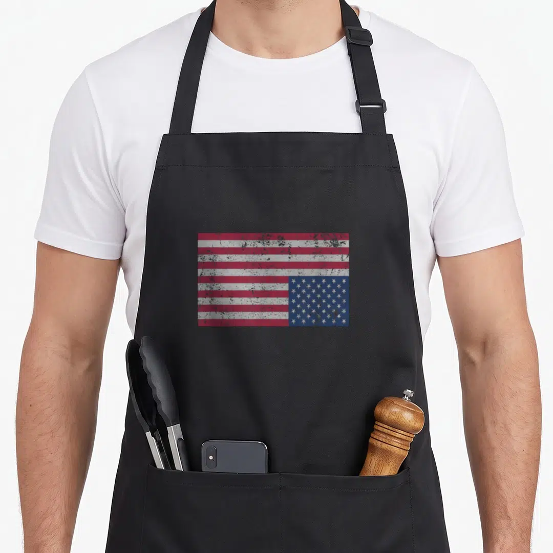 Upside american flag apron - Distressed red white and blue flag with stars in bottom right corner — shown on a black cotton canvas apron against a white background