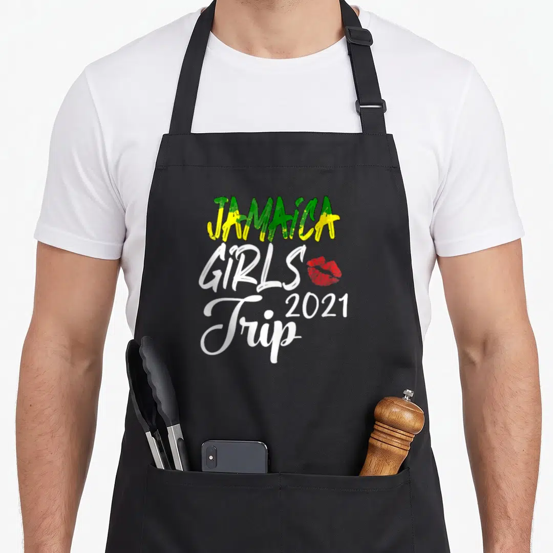 Jamaica girls trip apron - Stacked JAMAICA GIRLS Trip 2021 text in green yellow white red with red lip print — shown on a black cotton canvas apron against a white background