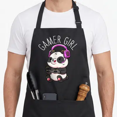 Panda video game apron - Cartoon panda wearing pink headphones and holding a controller under arched Gamer Girl text — shown on a black cotton canvas apron against a white background