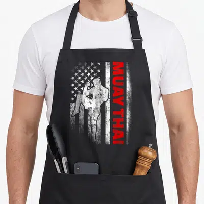 Muay american flag apron - Distressed USA flag with fighter silhouette and vertical MUAY THAI text in red white blue — shown on a black cotton canvas apron against a white background