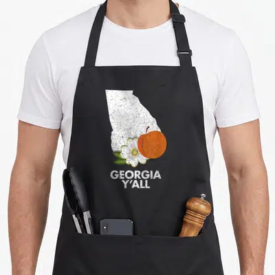 State georgian girl apron - White Georgia map silhouette with orange peach and green flower leaves and text GEORGIA — shown on a black cotton canvas apron against a white background