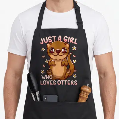 Funny river otter apron - Cartoon brown otter sitting among pink hearts and white flowers with arched pink text above — shown on a black cotton canvas apron against a white background