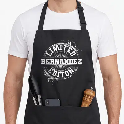 Hernandez family reunion aprons - White distressed circular seal with Limited Hernandez Editon text and paint splatters — shown on a black cotton canvas apron against a white background