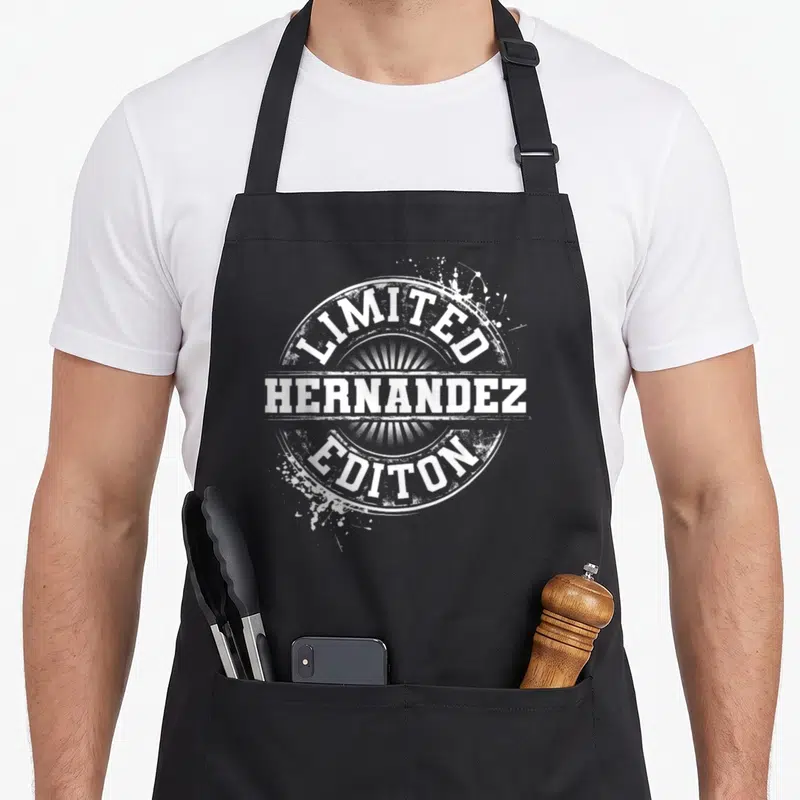Hernandez family reunion aprons - White distressed circular seal with Limited Hernandez Editon text and paint splatters — shown on a black cotton canvas apron against a white background