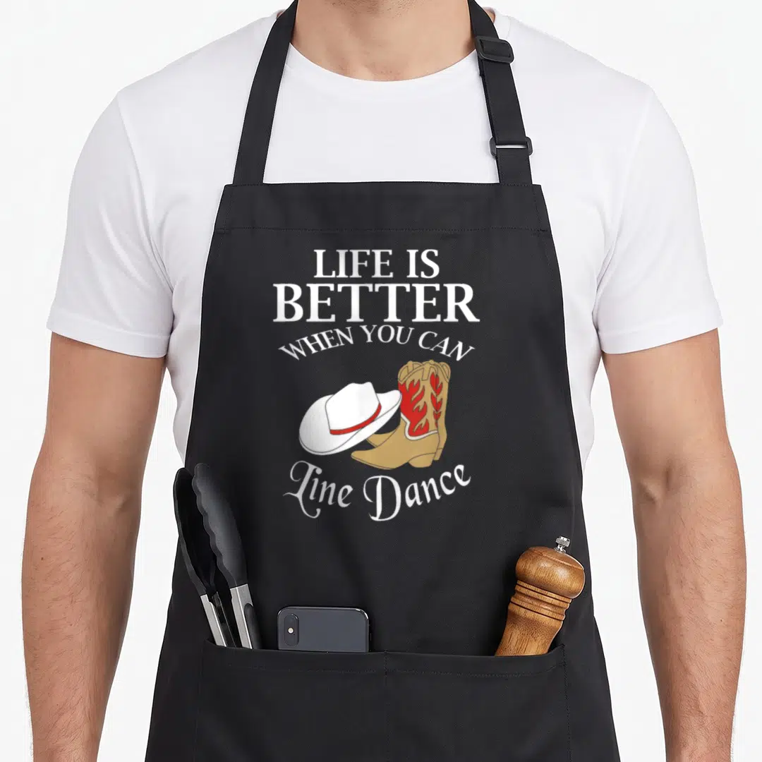 Cal country apron - LIFE IS BETTER WHEN YOU CAN LINE DANCE text with tan boots and white hat graphic — shown on a black cotton canvas apron against a white background