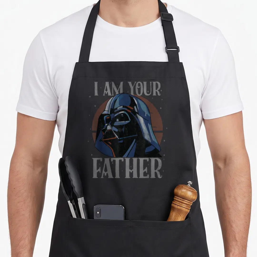 Cute father falcon dad apron - Darth Vader head over red circle with I AM YOUR FATHER text in distressed blue and grey — shown on a black cotton canvas apron against a white background