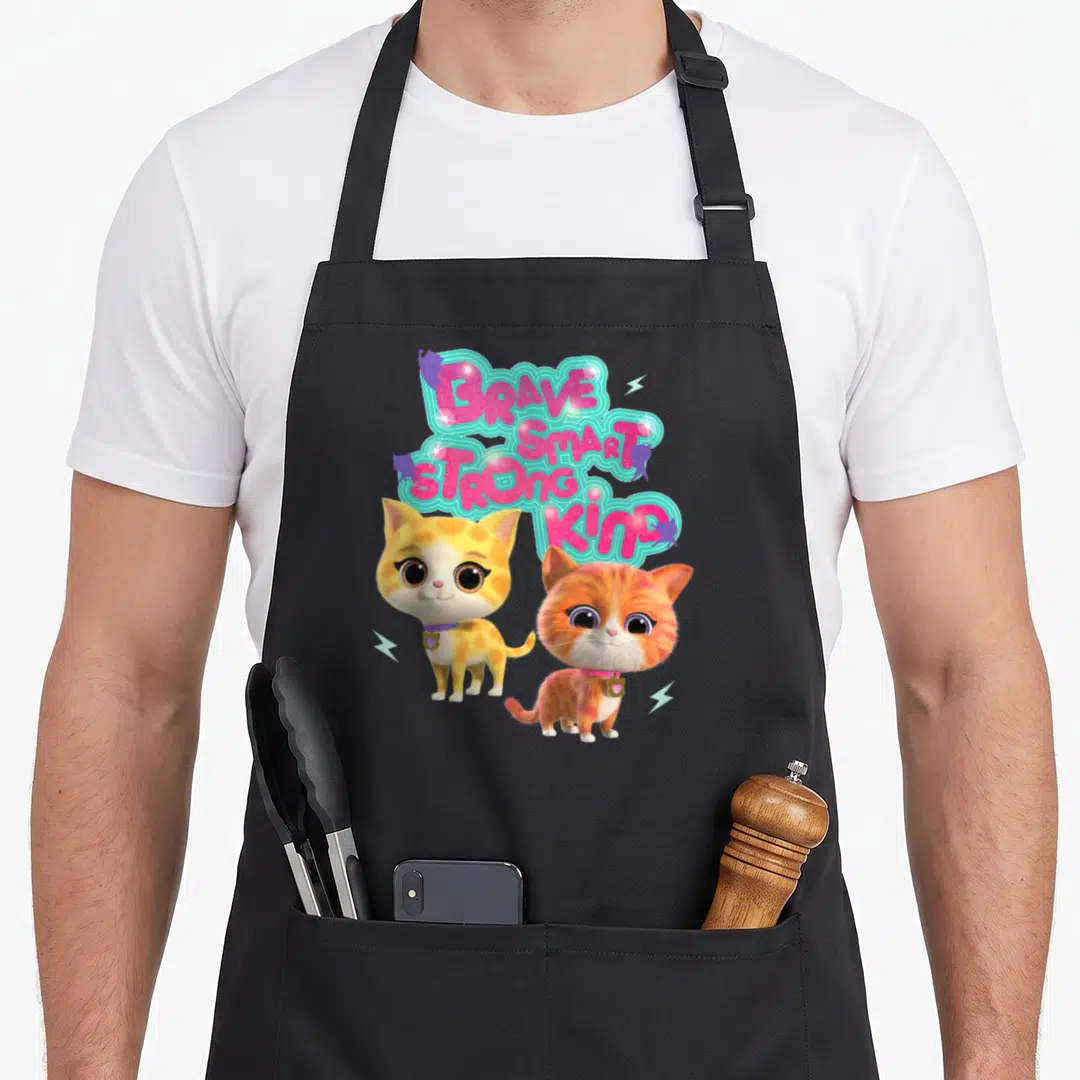 Brave junior apron - Two cartoon kittens below stacked pink words brave smart strong kind with teal outline — shown on a black cotton canvas apron against a white background