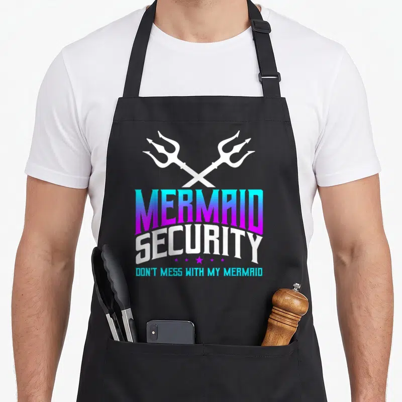 Merdad grill daddy apron - Crossed white tridents above gradient text reading MERMAID SECURITY DON'T MESS WITH MY — shown on a black cotton canvas apron against a white background