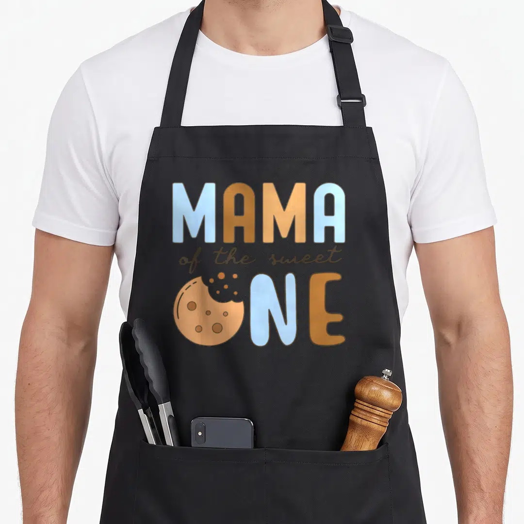 Mama cookies apron - Cartoon cookie replacing O in MAMA of the sweet ONE text in blue and brown — shown on a black cotton canvas apron against a white background