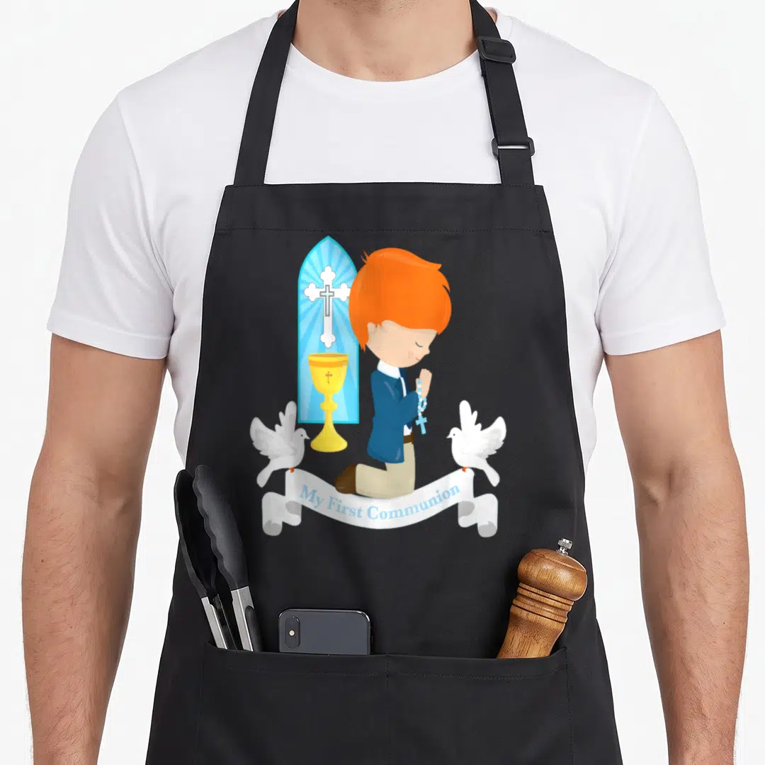 Redhead communion aprons - Cartoon boy kneeling with chalice and doves, My First Communion banner text — shown on a black cotton canvas apron against a white background