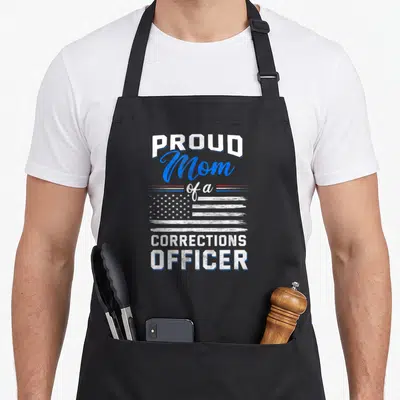 Proud officer mom apron - PROUD Mom of a CORRECTIONS OFFICER text with distressed flag in white blue and red — shown on a black cotton canvas apron against a white background