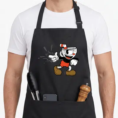 Cuphead snap aprons - Cartoon cup-headed character pointing left with action lines in red, black, white, and brown — shown on a black cotton canvas apron against a white background