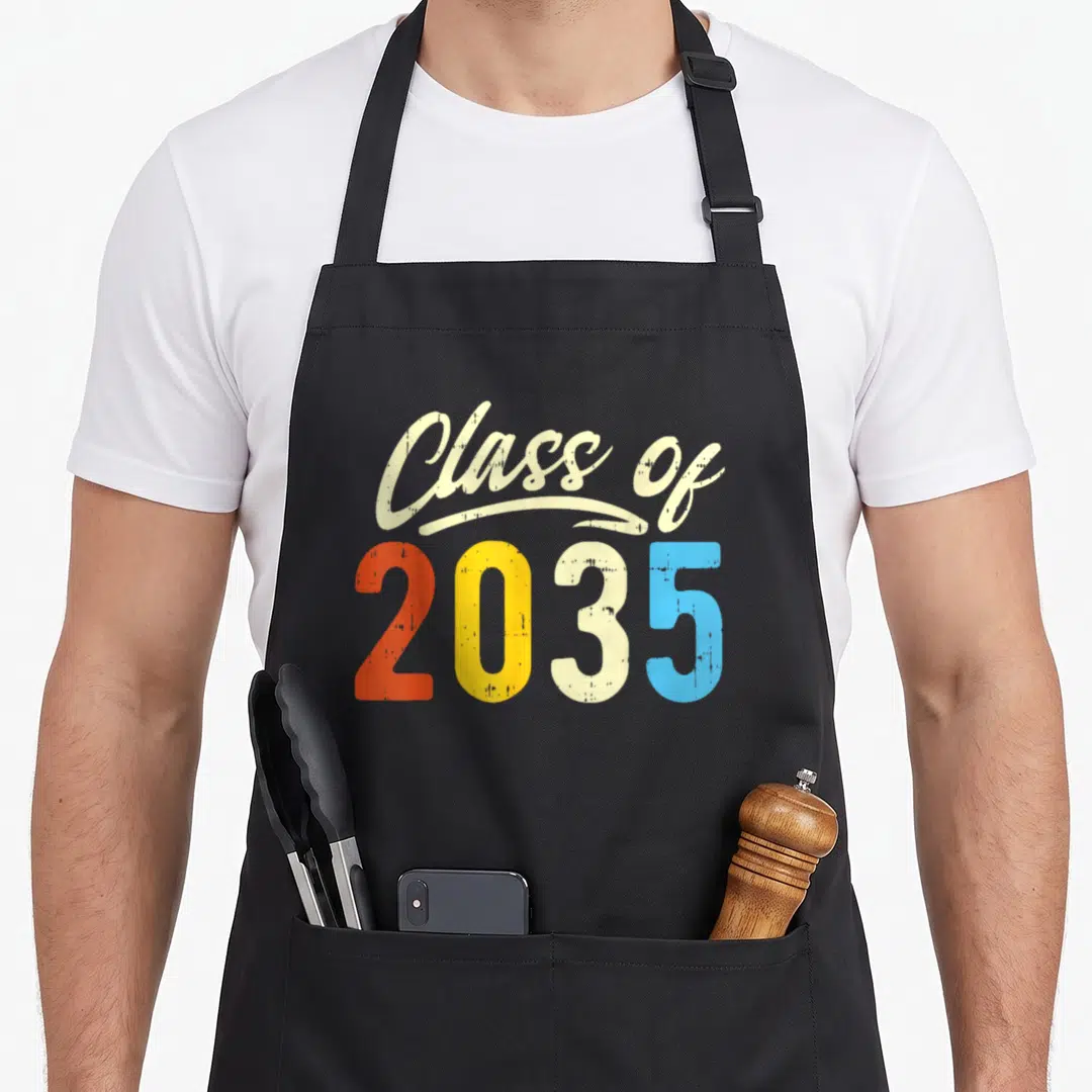 Grow kindergarten apron - Class of 2035 retro typography in cream orange yellow and light blue — shown on a black cotton canvas apron against a white background