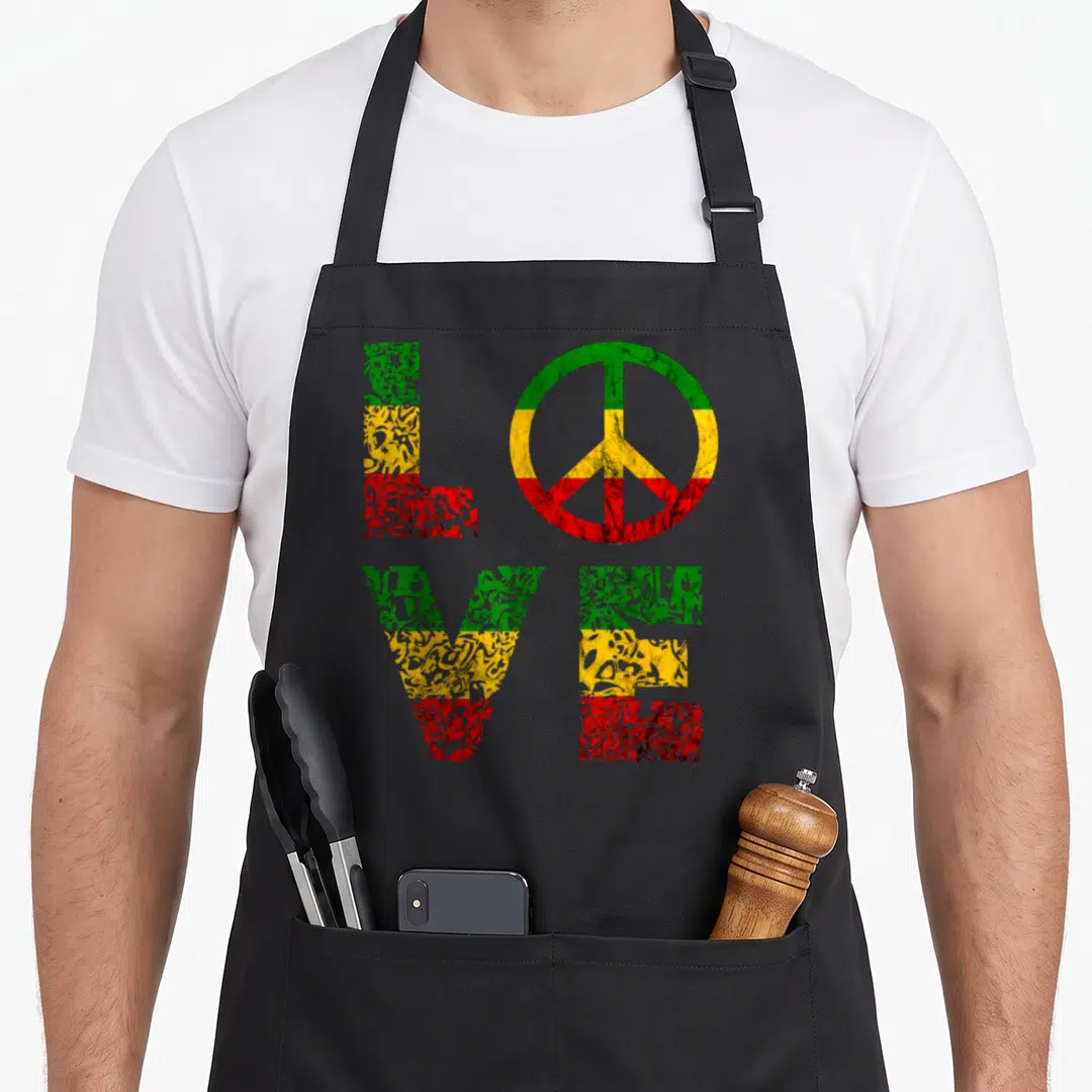 Reggae hippie apron - Distressed LOVE text with peace symbol filled in green yellow red stripes — shown on a black cotton canvas apron against a white background