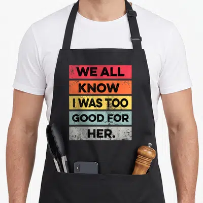Funny divorced divorce party apron - Stacked colorful text blocks reading WE ALL KNOW I WAS TOO GOOD FOR HER in bold — shown on a black cotton canvas apron against a white background