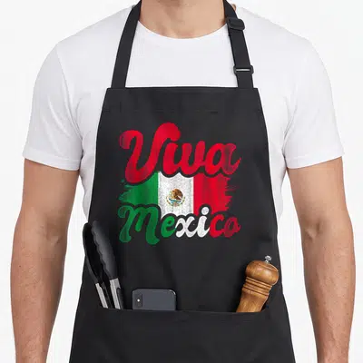 Viva mexican apron - Viva Mexico script over distressed green white red flag with eagle emblem — shown on a black cotton canvas apron against a white background