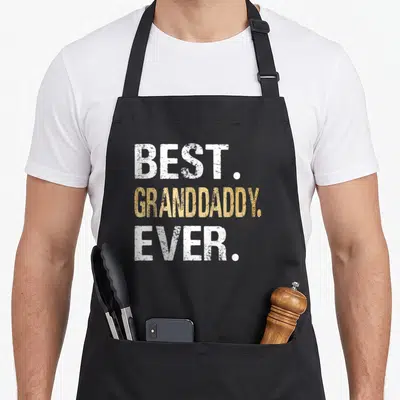Granddaddy grandpa apron - White and gold stacked text reading BEST GRANDDADDY EVER on grey background — shown on a black cotton canvas apron against a white background