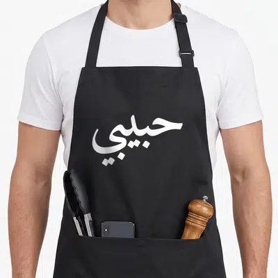 Arabic letter arab apron - White Arabic calligraphy reading Habibi centered on gray background — shown on a black cotton canvas apron against a white background