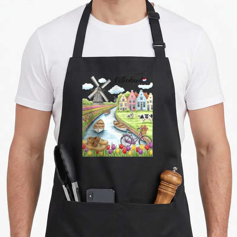 Windmill tulip apron - Netherland text flag windmill canal cows clogs purple bicycle tulips watercolor — shown on a black cotton canvas apron against a white background