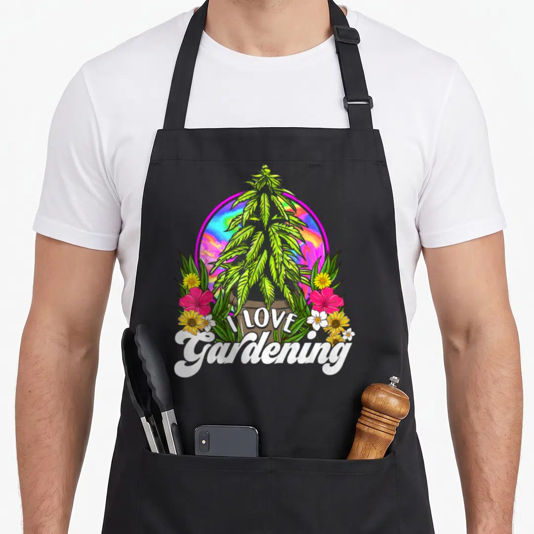 Marijuana i love hemp apron - Cartoon cannabis plant in pot with I LOVE Gardening text and multicolored floral border — shown on a black cotton canvas apron against a white background