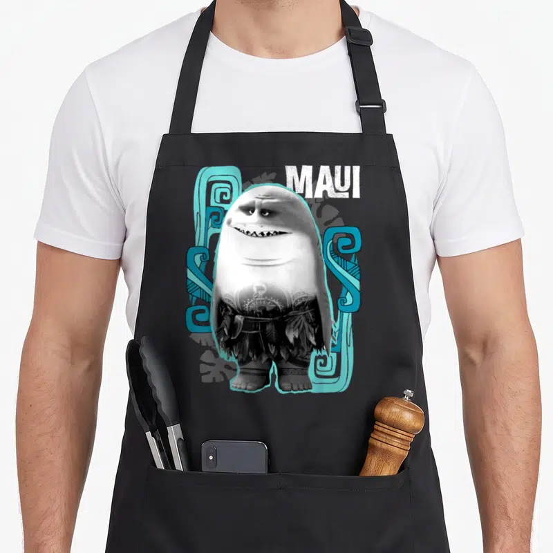 Shark novelty apron - Cartoon half-shark character with tribal tattoos and leaf skirt surrounded by blue patterns — shown on a black cotton canvas apron against a white background