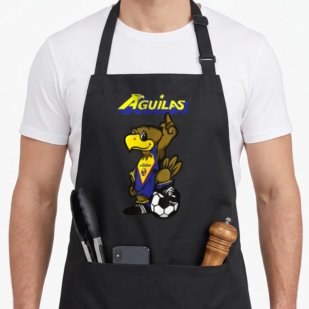 Exclusive collection apron - AGUILAS banner above cartoon eagle in blue jersey standing on soccer ball pointing up — shown on a black cotton canvas apron against a white background