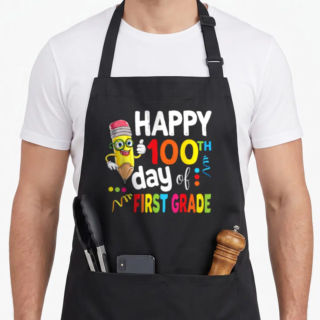 Retro 100th teacher apron - Cartoon pencil with glasses next to Happy 100th Day of First Grade text in multiple colors — shown on a black cotton canvas apron against a white background