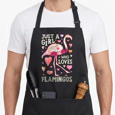 Flower the floral apron - Flamingo filled with flowers and hearts with text Just A Girl Who Loves Flamingos — shown on a black cotton canvas apron against a white background