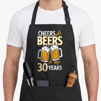 Cheer beer apron - Two orange beer mugs clinking below text reading Cheers and Beers to my 30 Years — shown on a black cotton canvas apron against a white background