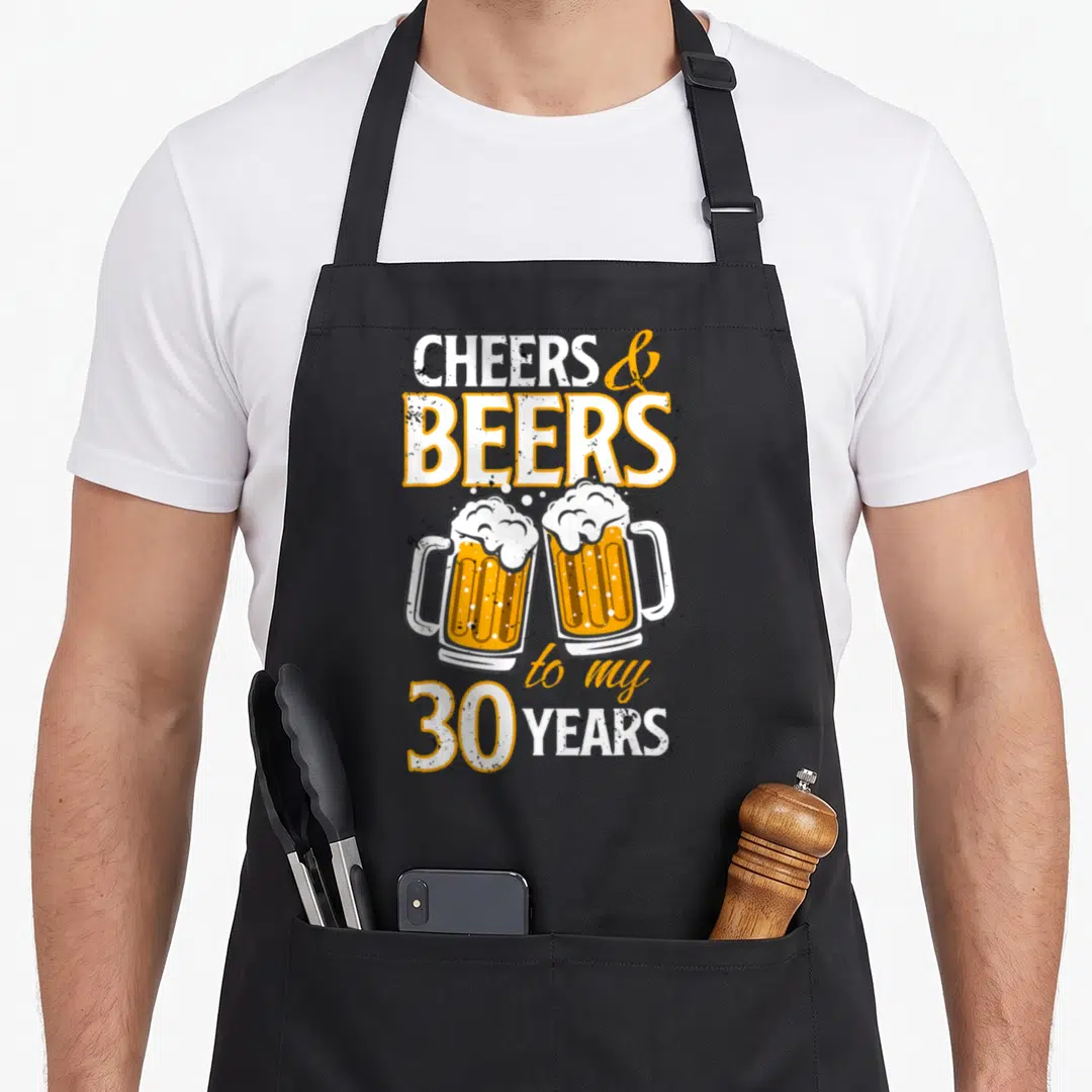 Cheer beer apron - Two orange beer mugs clinking below text reading Cheers and Beers to my 30 Years — shown on a black cotton canvas apron against a white background