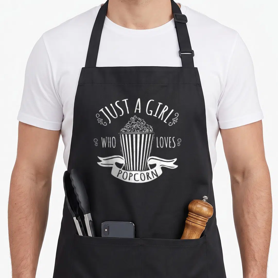 Popcorn golf fan apron - Distressed white text Just A Girl Who Loves Popcorn over striped bucket with ribbon banner — shown on a black cotton canvas apron against a white background
