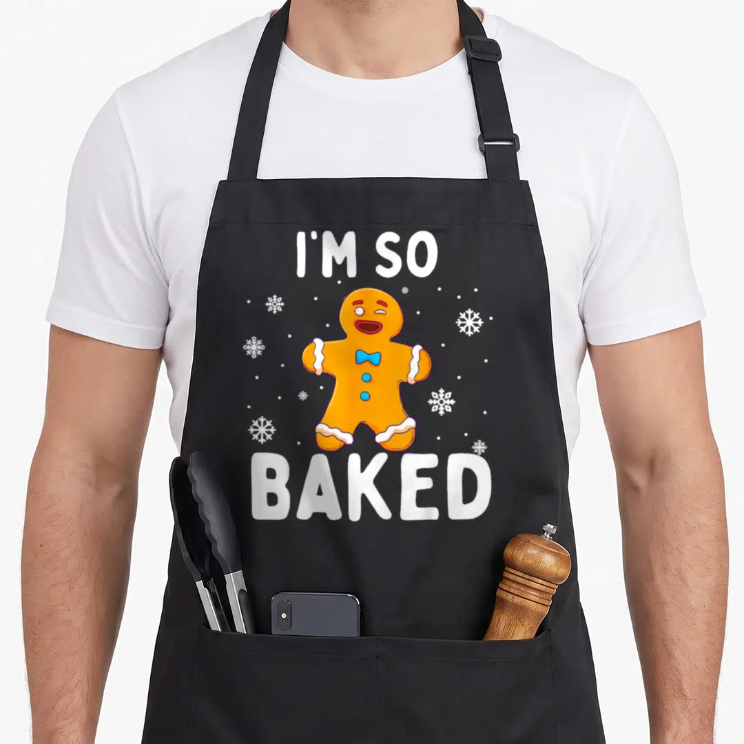 Baked christmas cookie apron - Orange gingerbread man with blue bow tie and I'M SO, BAKED text — shown on a black cotton canvas apron against a white background