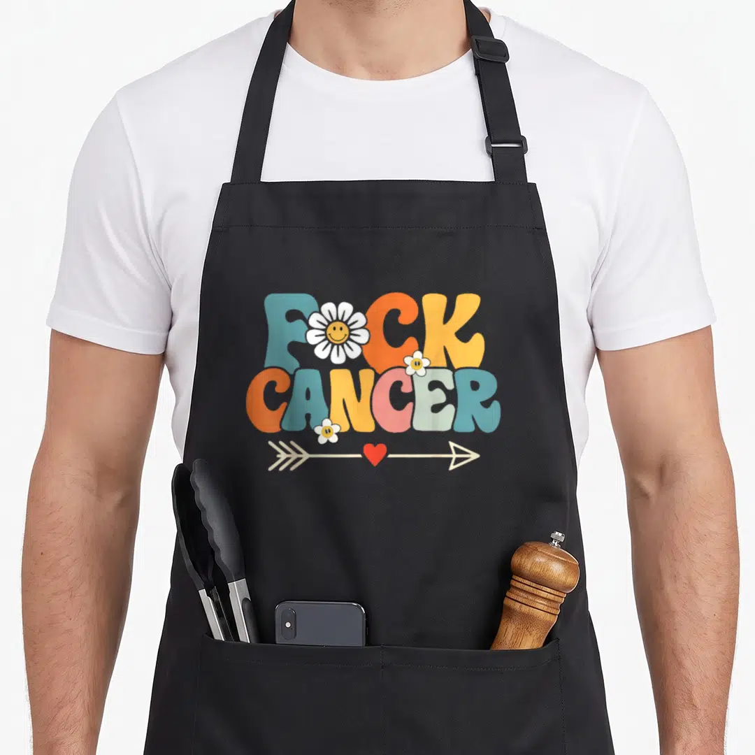 Groovy breast cancer awareness aprons - FUCK CANCER text in blue orange pink yellow with smiley daisies and heart arrow — shown on a black cotton canvas apron against a white background