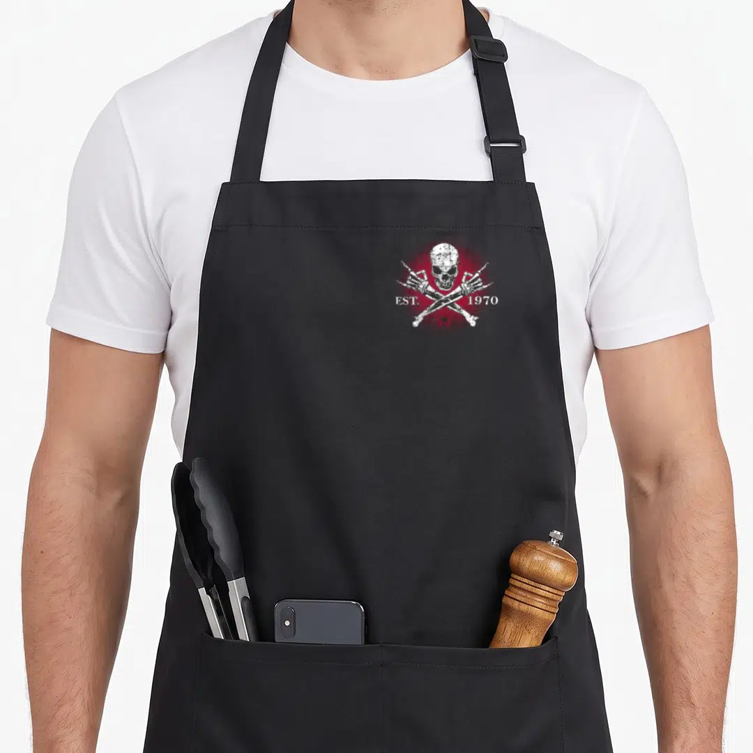 Gen skull apron - Distressed white skull and crossbones with red star and EST 1970 text — shown on a black cotton canvas apron against a white background