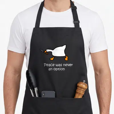 Peace option meme apron - Cartoon goose holding knife above text Peace was never an option — shown on a black cotton canvas apron against a white background