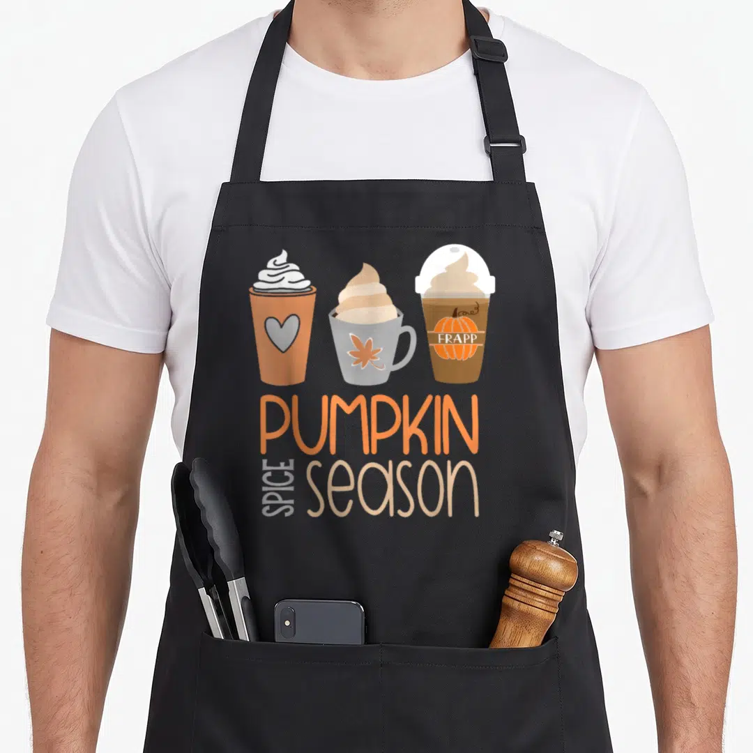 Spice fall aprons - Three cartoon coffee cups above stacked PUMPKIN SPICE season text in orange and beige — shown on a black cotton canvas apron against a white background